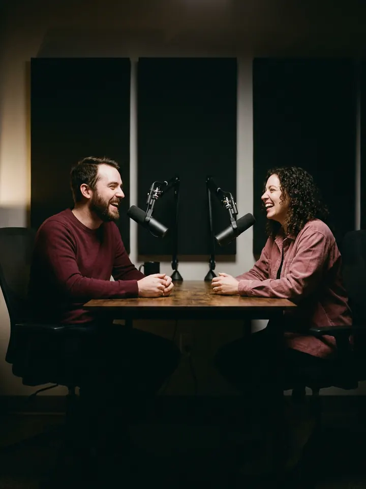 Two podcast hosts laughing in a studio